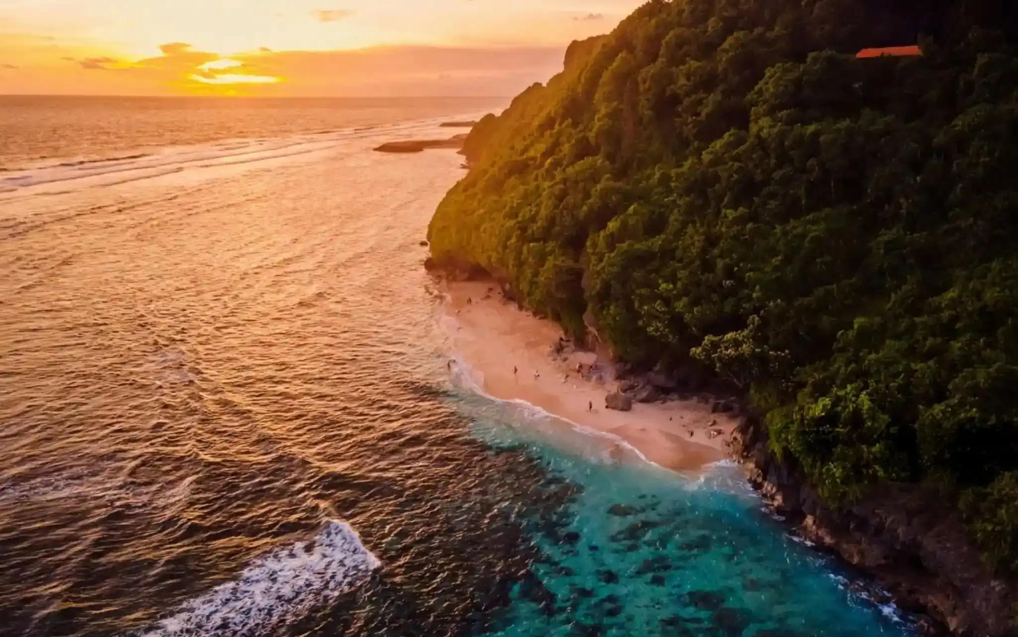 An aerial view of Green Bowl Beach in Bali at sunset, showing the turquoise ocean next to a sandy beach and a lush green cliffside.