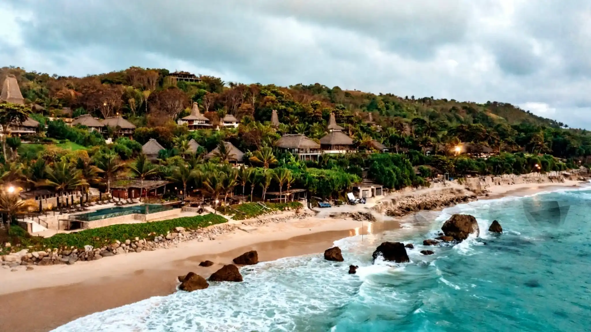 Panoramic view of Nihi Sumba resort near Sumba Estate, showing beachfront villas, pool, and lush tropical hillside.